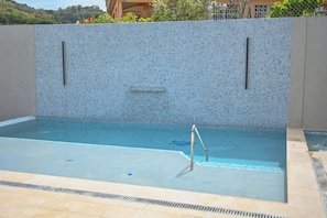 Una piscina con pared de azulejos, escalera de metal y superficie de agua azul cristalina.