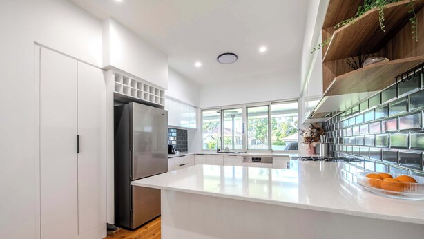 Une cuisine moderne avec des meubles blancs, un réfrigérateur en acier inoxydable, un grand îlot central et une vue sur l’extérieur.