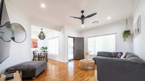 Un salon moderne avec un canapé gris, un plancher en bois, un ventilateur de plafond et un coin repas comprenant une table et des chaises.