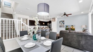 Ein modernes Wohnzimmer mit Essbereich, grauem Sofa, gedecktem Esstisch und einer Küche im Hintergrund.