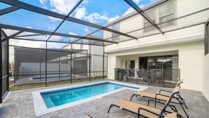 Ein Schwimmbecken mit Liegestühlen, einer überdachten Terrasse und einem verglasten Bereich.