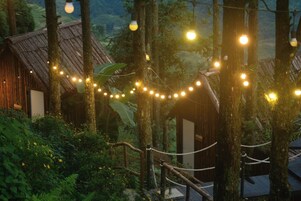 Una cabaña rústica rodeada de árboles, con luces colgantes.