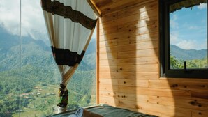 A wooden cabin room with a bed, a window, and a view of a mountainous landscape. - D Home Sapa 10 (Sa Pa)