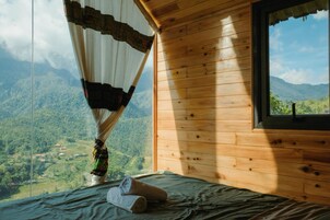 Una habitación de cabaña de madera con una cama, un ventanal y vistas a un paisaje montañoso.