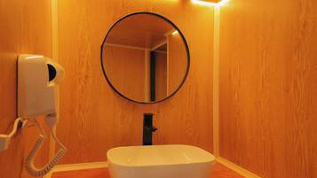 A bathroom with a wooden wall, a round mirror, a white sink, and a hairdryer.