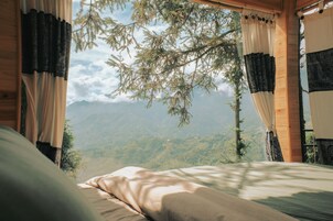 A bedroom with a bed, curtains, and a view of mountains.