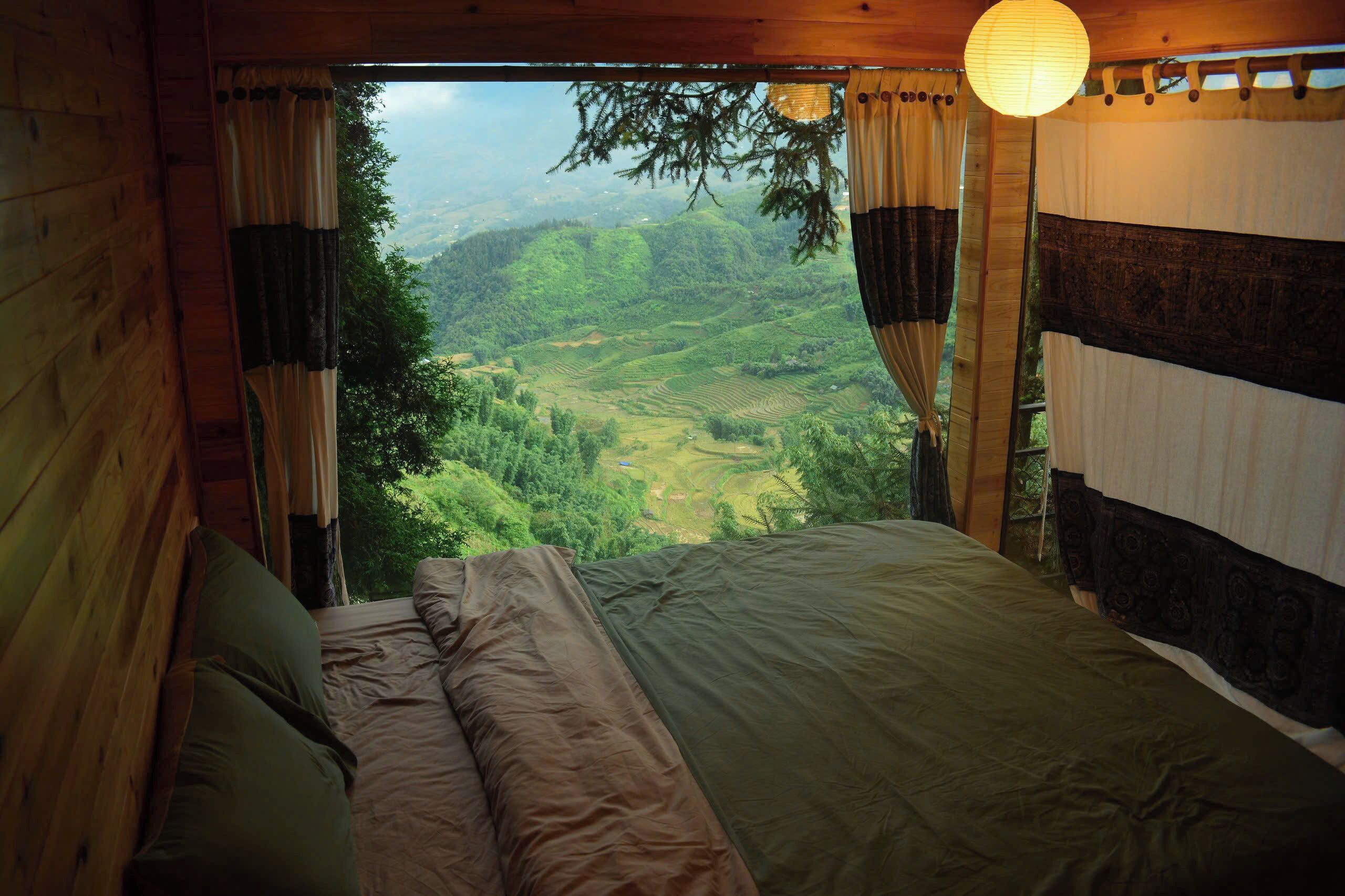 A bedroom with a large bed, wooden walls, and a view of a green valley.