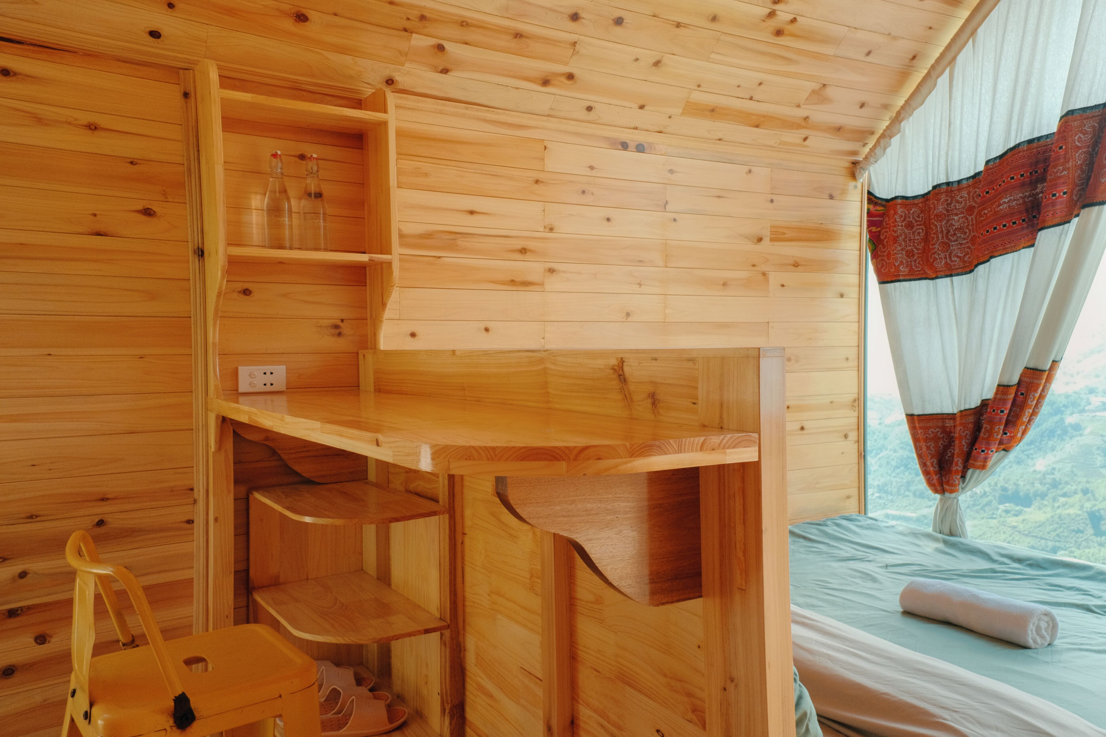 L'intérieur d'un chalet en bois, avec un lit, un bureau en bois et une chaise.