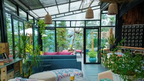 A spacious indoor area with a large glass door leading to an outdoor garden, featuring a blue sofa, a small round table, and various plants. - D Home Sapa 10 (Sa Pa)