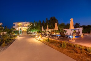 Un espacio exterior bien iluminado con piscina, sillas de descanso y sombrillas.