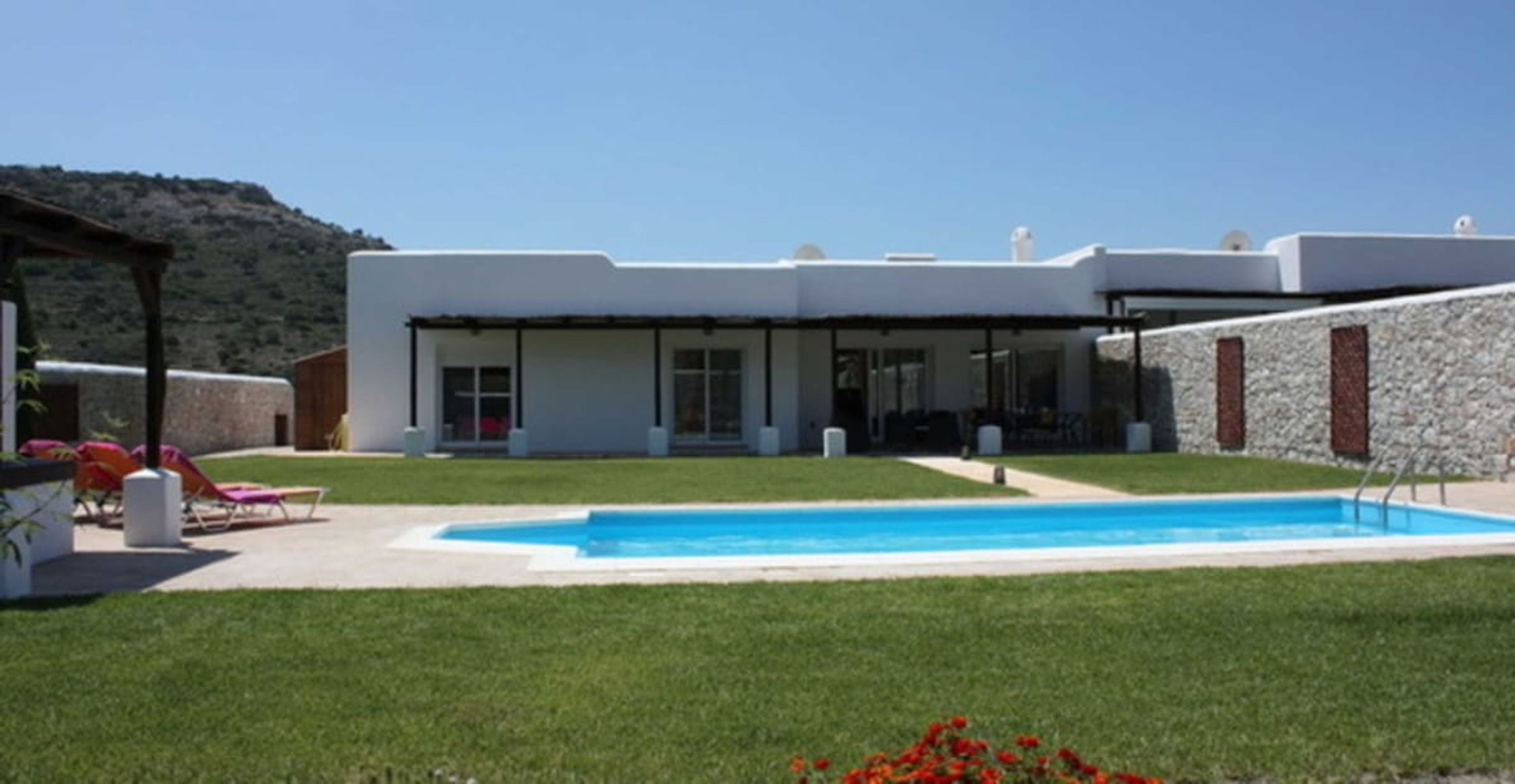 A modern house with a swimming pool, a covered patio, and a stone wall.
