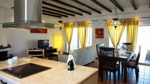 Una cocina moderna con una isla central, comedor con sillas, un sofá y una televisión.