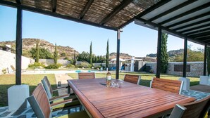 Un patio al aire libre con mesa y sillas de madera, una piscina y vistas a las colinas.