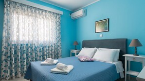 A bedroom with a bed, two bedside tables, a nightstand, a window with curtains, and an air conditioning unit. - The Rhodes South Escape Beach (Rhodes)