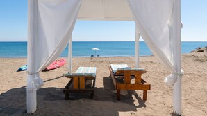 A beach setting with a white canopy structure, two wooden lounge chairs, and a red kayak on the sand. - The Rhodes South Escape Beach (Rhodes)
