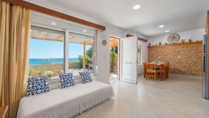 A bedroom with a large bed, a dining area with a table and chairs, and a view of the sea through a sliding glass door. - The Rhodes South Escape Beach (Rhodes)