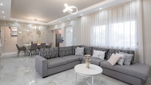 A modern living room with a grey sectional sofa, a round coffee table, and a dining area with a white table and chairs. - The Cottage South Escape With Beach Front Pool (Rhodes)
