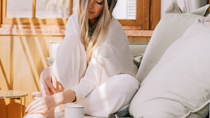 Eine Person sitzt auf einem Bett und hält ein Tablett mit Essen und Beilagen.