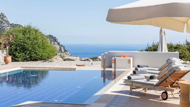 Un espace piscine doté de chaises longues et de parasols, offrant une vue sur une côte rocheuse et la mer.