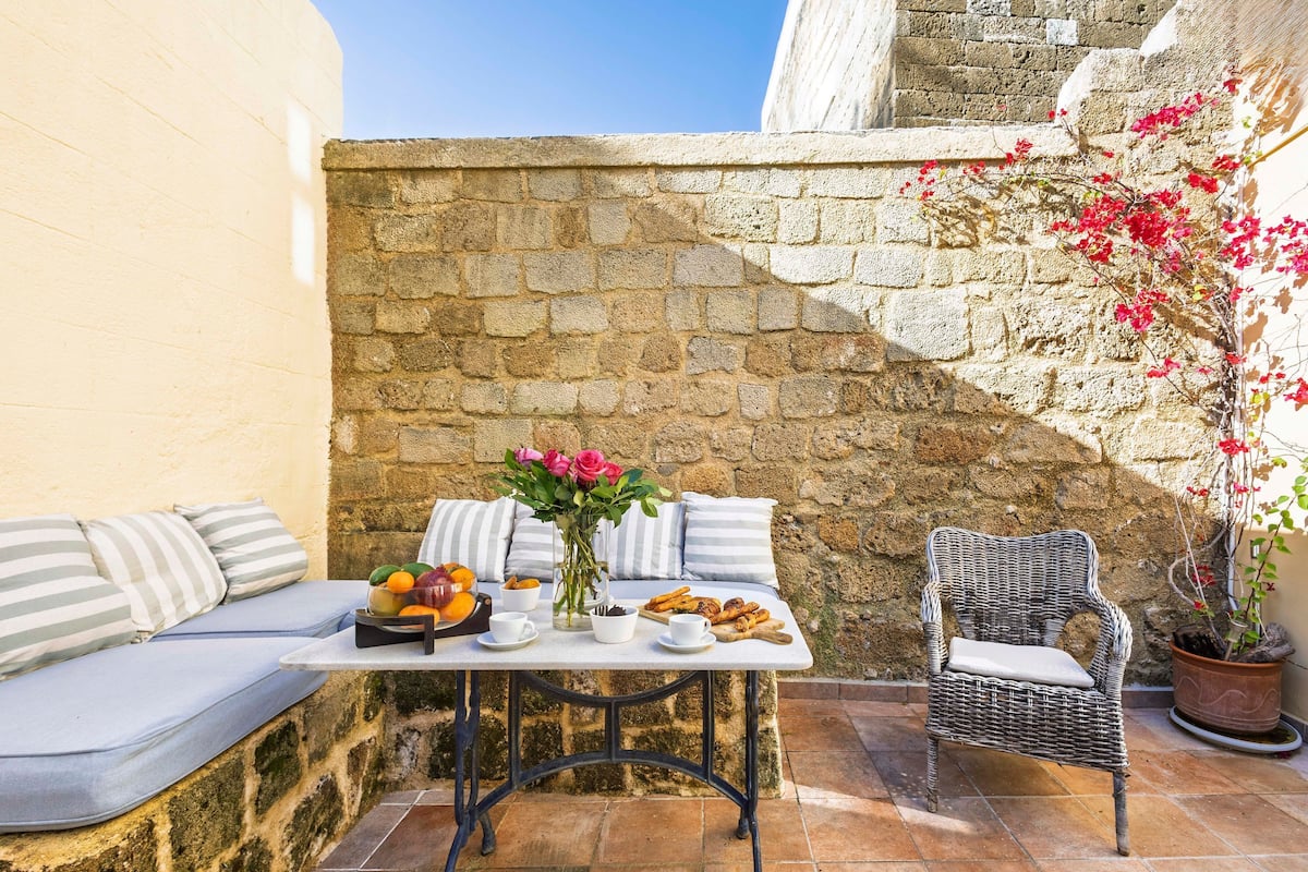 A stone wall, a wicker chair, a table with food and drinks, and a cushioned bench.