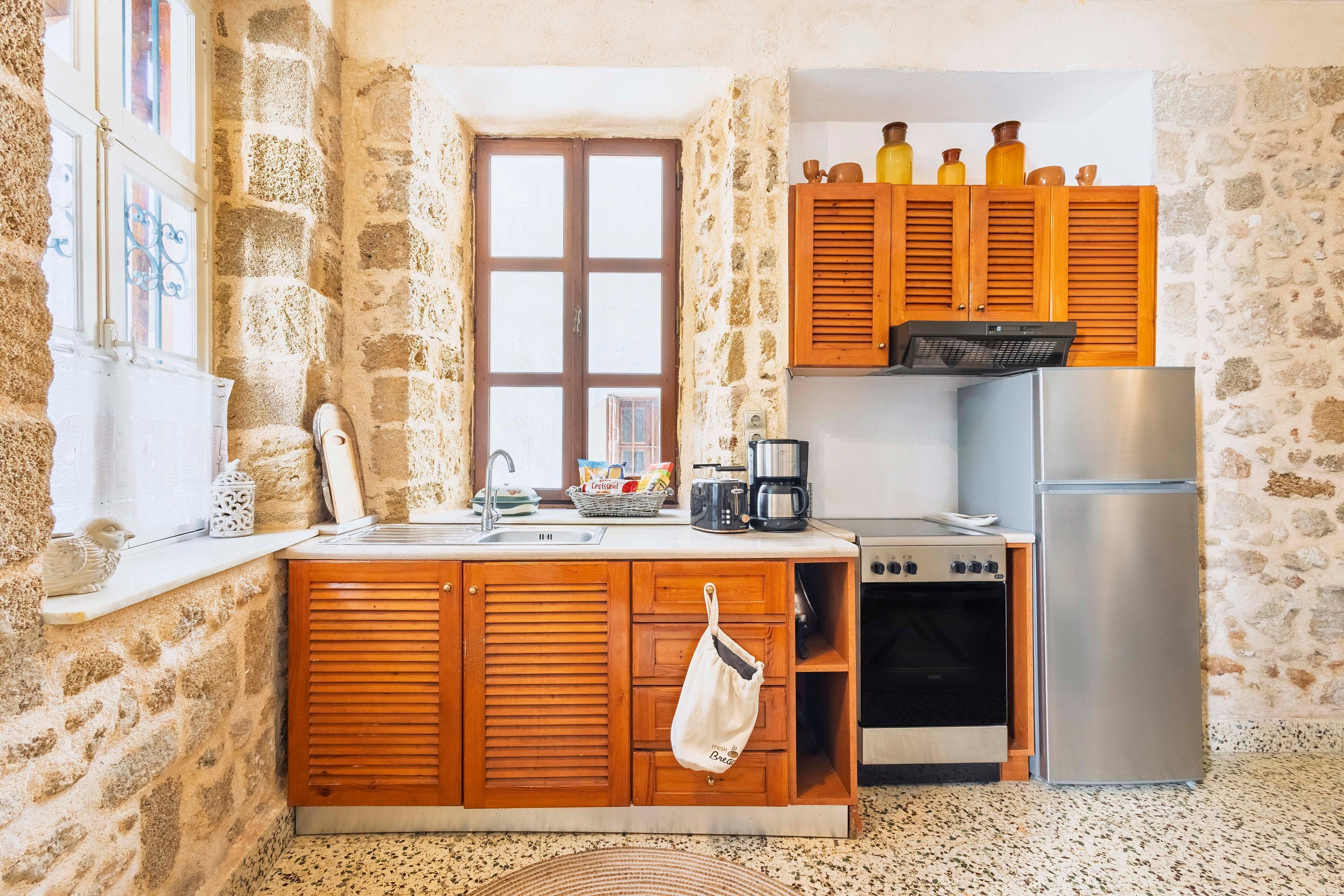 Une cuisine compacte avec des murs en pierre, des armoires en bois, un réfrigérateur en acier inoxydable et une fenêtre offrant une vue agréable.