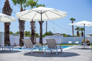 Ein Poolbereich mit Liegestühlen und Sonnenschirmen, Palmen und einem klaren Himmel.