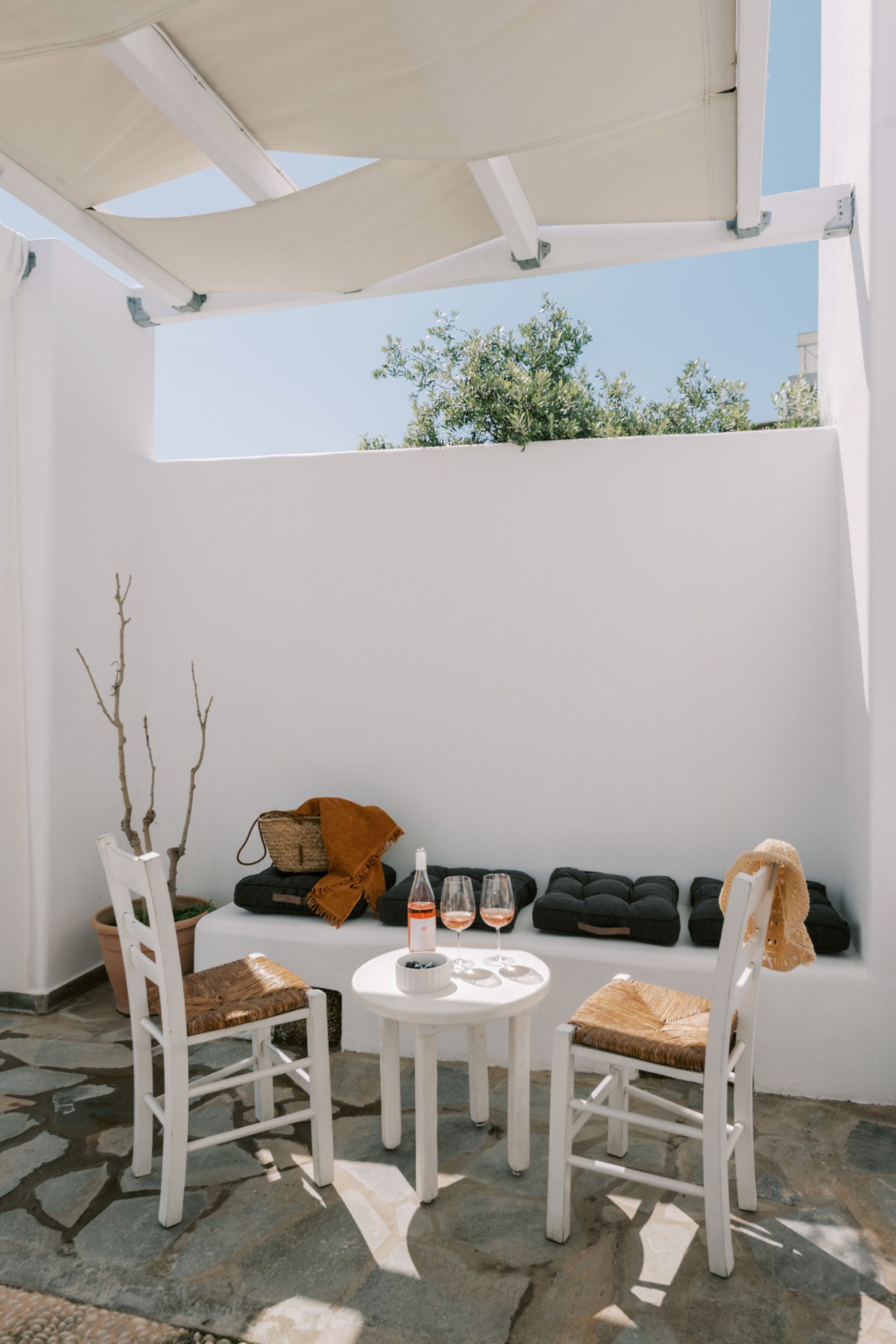 A white outdoor seating area with two white chairs, a small round table, and a bench with cushions.