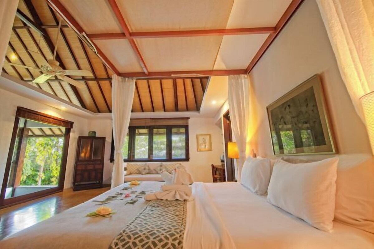 Een hotelkamer met een groot bed, een plafondventilator en uitzicht op groen.
