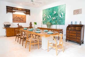 Een eethoek met een houten tafel, stoelen en een groot, abstract groen schilderij aan de muur.