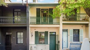 Une rangée de maisons de ville avec des balcons, des volets verts et un ciel dégagé.