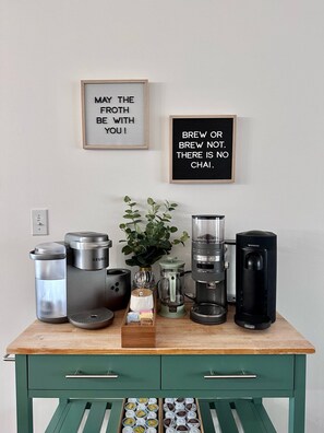 Una estación de café con diferentes equipos de preparación, una cita inspiradora en un marco y una planta en maceta.