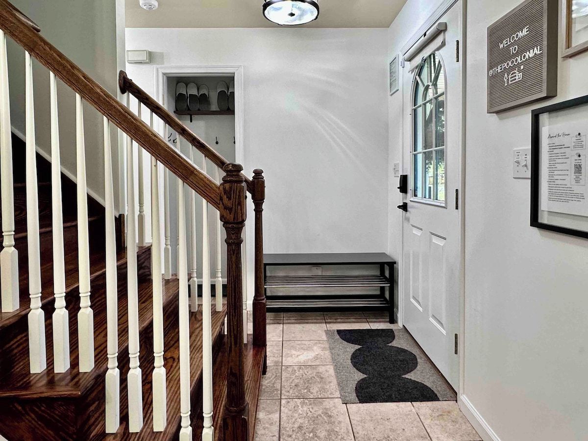 A hallway with a wooden staircase, a door with a shoe rack, and a welcome sign.