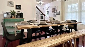 Een eetgedeelte met een houten tafel voor vier personen, zwarte stoelen, een groene buffetkast en een kroonluchter.