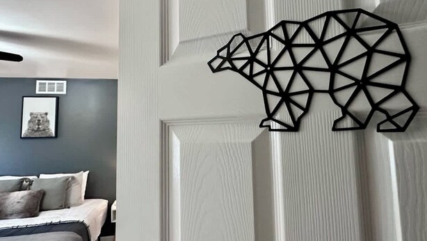 Een kamer met een bed, een geometrische beren decoratie aan de muur en een ingelijst foto.