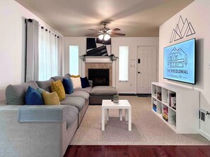 A living room with a sofa, a fireplace, a ceiling fan, a television, and a bookshelf. - Pocolonial Charming 4BR Mountain Retreat (Albrightsville)