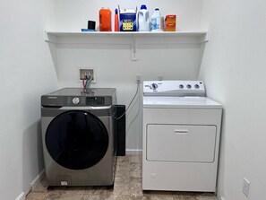 A laundry area with a Samsung washer and dryer, a shelf with cleaning supplies, and a tiled floor. - Pocolonial Charming 4BR Mountain Retreat (Albrightsville)