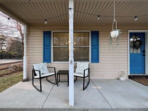 A covered porch with two chairs and a table, a white column, and a blue door. - Pocolonial Charming 4BR Mountain Retreat (Albrightsville)