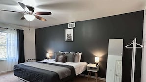 Een slaapkamer met een bed, nachtkastjes, een plafondventilator, een spiegel en een raam met gordijnen.