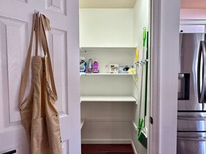 A kitchen with a stainless steel refrigerator, a white door with a beige apron hanging, and a shelf with cleaning supplies. - Pocolonial Charming 4BR Mountain Retreat (Albrightsville)