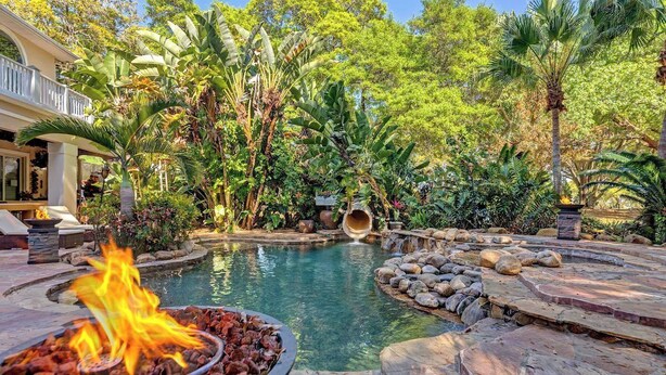 Una piscina rodeada de plantas tropicales y una chimenea decorativa.