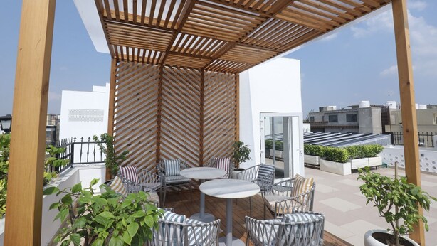 Een overdekt terras met een houten pergola, rieten meubels en potplanten.