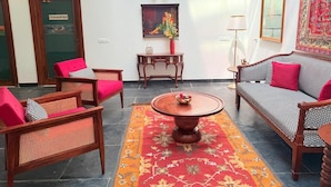 Een ruime lobby met een ronde houten salontafel, twee banken met rode kussens, en een vloerkleed met een patroon.