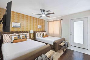 A hotel room with two beds, a ceiling fan, a television, and a door with a view.