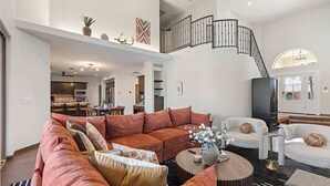 Een ruime woonkamer met een grote hoekbank, een ronde salontafel en een trap met een zwarte leuning.
