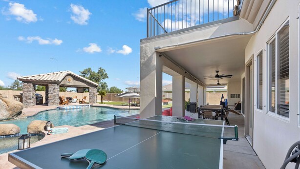 Een pooltafel met een tennisracket, een terras met tuinmeubilair en uitzicht op een zwembad en een gebouw met balkon.