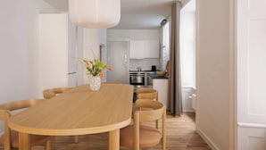 A modern dining area with a wooden table and chairs, a hanging light fixture, and a view into the kitchen. - Chic city pad - Handpainted art - Great location by Daniel&Jacob's (København)