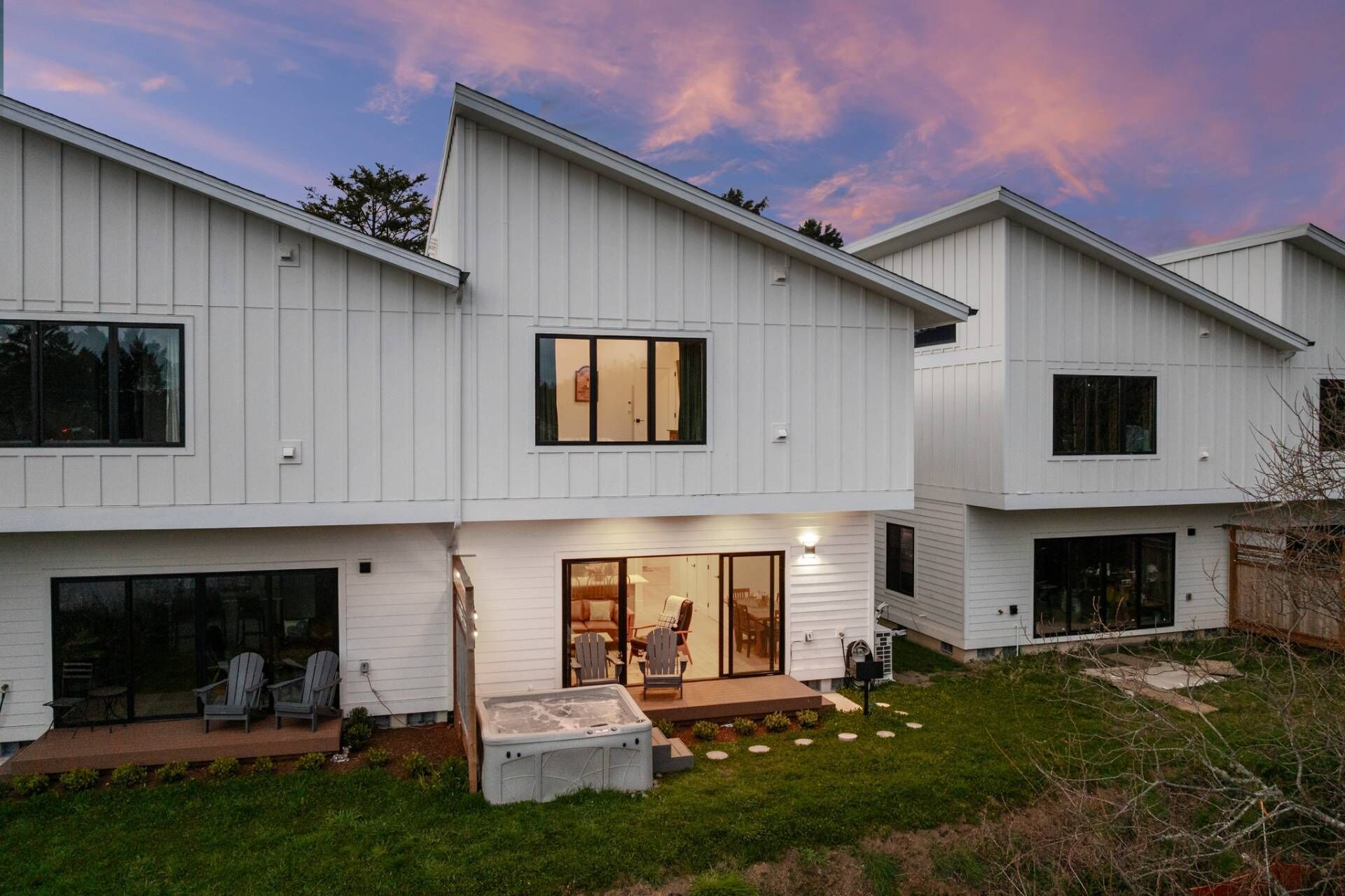 A modern two-story house with a patio area, outdoor seating, and a hot tub.