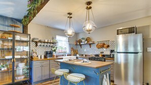 A modern kitchen with a central island, bar stools, a stainless steel refrigerator, and hanging kitchen utensils.