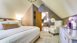 A bedroom with a large bed, a dresser, and a chair. There is a door leading to another room.
