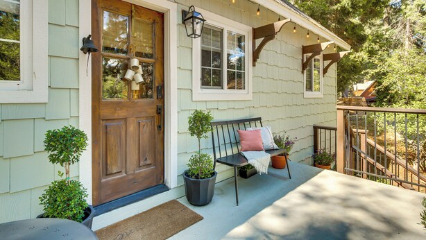 A porch with a wooden bench, potted plants, and a door.